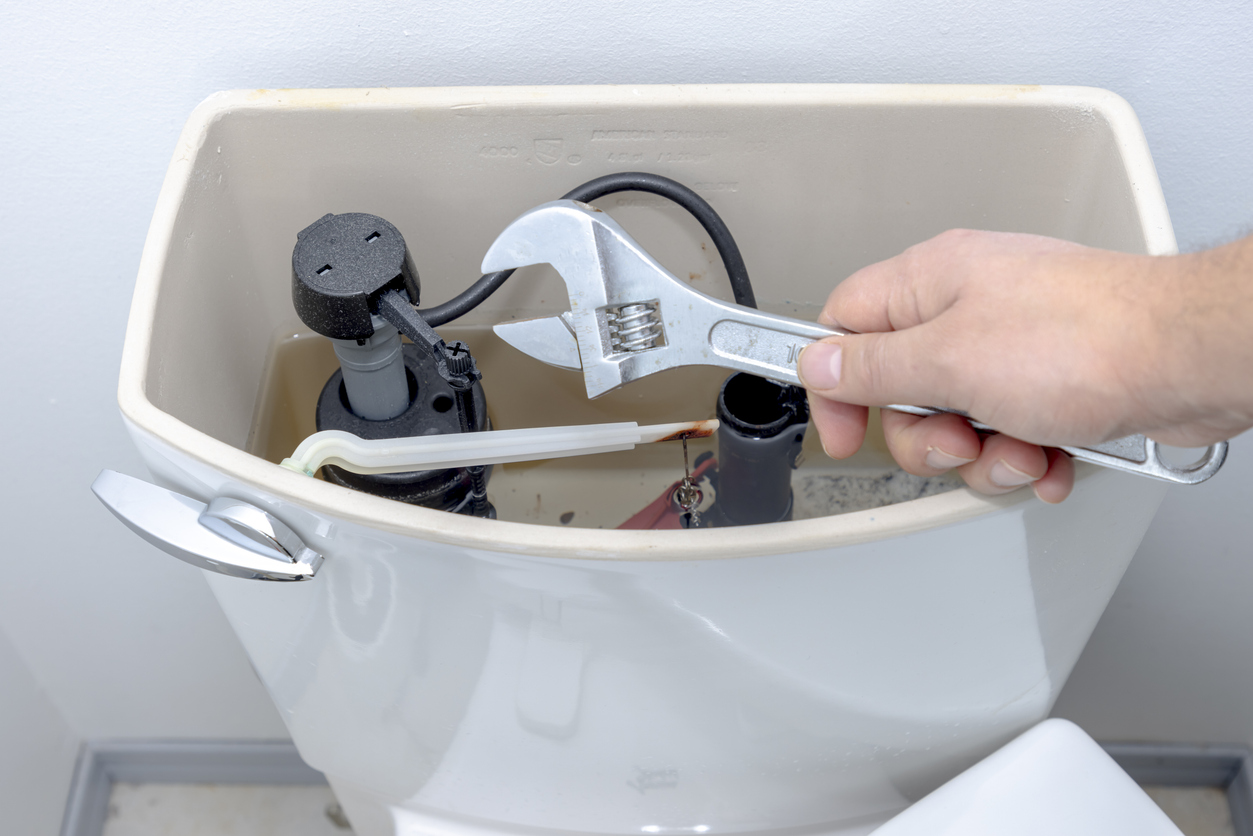 A hand using a wrench to adjust parts inside a toilet tank during a toilet repair in Sacramento.